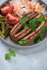 Close-up of roasted sausages with sauerkraut, gherkins, tomatoes and fresh parsley, selective focus, vertical shot