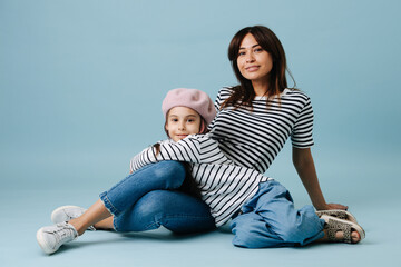 Cute mom and daughter sitting on floor, posing for a photo, wearing same clothes
