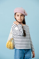 Portrait of a fashionable little girl in french beret holding bag with bananas