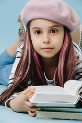 Thoughtful little girl in french beret lying on the floor, reading book