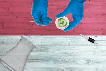 Indonesia flag on laboratory table. Medical healthcare technologist holding COVID-19 swab collection kit, wearing blue protective gloves, epidemic concept.