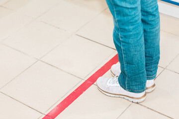 Person stand in line, legs close-up. Attention line on the floor of the store to maintain social distance. Concept of the coronavirus pandemic and prevention measures