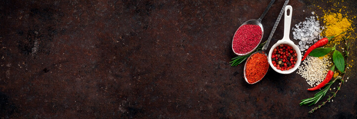 Spices on a dark rusty background, pepper, Basil, salt, rosemary, thyme, turmeric. herbs and greens...