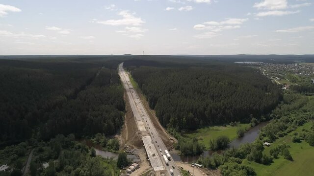 8. Aerial view of bridge repair over the river and construction works of a highway section. Cars are going from both sides. The scheme of transport movement has changed. Road goes through the forest