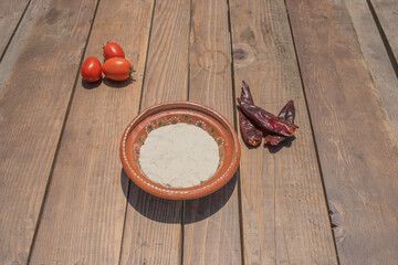 dough for Mexican tortillas in clay plate on table with chili peppers and tomatoes