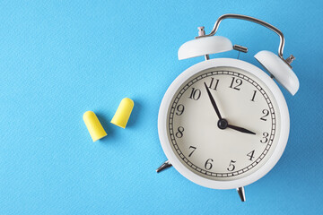 Insomnia problem concept. Alarm clock and ear plugs on a blue background, top view