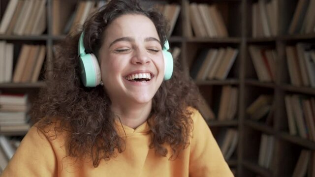 Happy positive latin teenage girl laughing at funny joke looking at camera in library. Cheerful hispanic teen school college student wear headphones having fun, smiling ethnic face close up portrait.