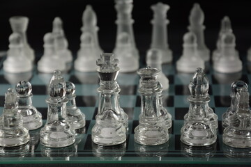 Clear glass chess pieces on a glass chessboard isolated on a black background