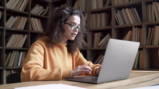 Smiling young hispanic teen girl college student using laptop computer typing on pc working from home office or studying on tech device in classroom sit at desk. Online education, elearning concept.