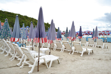 Beach chairs or sun loungers and umbrellas on the sandy seashore at Koh Larn island, Pattaya, Thailand. Using for a traveler to relax on a perfect vacation summer holiday at a tropical resort.