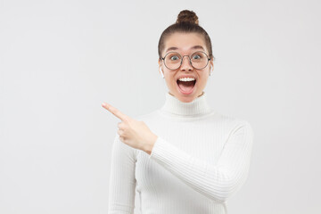 Wow! Young excited girl surprised with beneficial commercial offer or sales, pointing with finger to the left, isolated on gray background