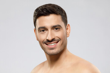 Fototapeta premium Close-up of young man with short haircut and stubble, standing with naked shoulders, concept of male beauty, isolated on gray background