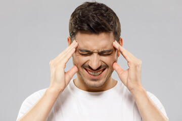 Close-up portrait of man touching temples with closed eyes, trying to relieve strong headache, feeling stressed and exhausted, isolated on gray background