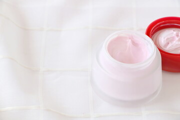 Close up pink cream in glass container on white fabric background, side view and have copyspace, look soft.