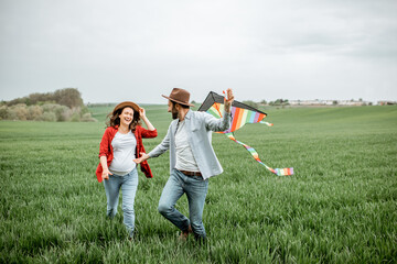 Happy couple having fun together, playing with kite on the greenfield. Happy couple expecting a baby and young family concept