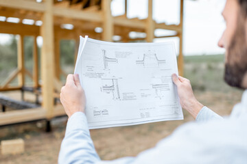 Builder looking on teh drawings of wooden house structures on the construction site. Concept of...