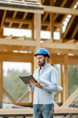 Portrait of an architect or builder with digital touchpad in front of the wooden house structure....