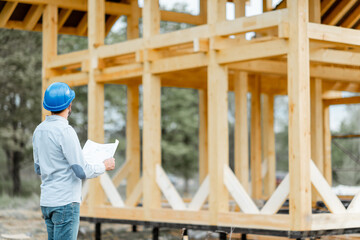 Builder or architect in hard hat supervising a project, standing with blueprints on the...