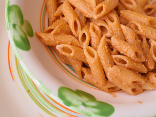 Lunchtime at home. First course of pasta with Sicilian pesto prepared with tomatoes, walnuts and ricotta cheese served on a green plate.