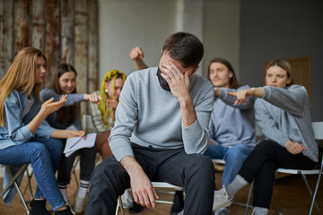 people humiliate and offend young sick man in mask. group of young people sit in the background and...