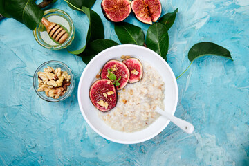 A bowl of porridge with figs slices and walnuts  on blue background. Flat lay. Copy space. Top view. Healthy breakfast.