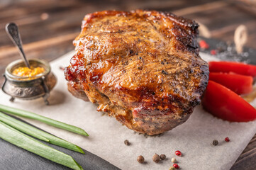 Homemade baked piece of meat with vegetables and spices on a serving board on a wooden table. Close up. Selective focus