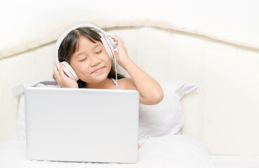 Cute happy Asian girls wearing headphones to listen music from laptop