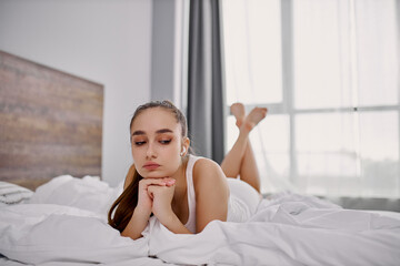 sad young woman has melancholic mood while listening to music on bed, woman enjoy lying in the morning.