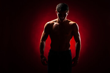 Fototapeta na wymiar Athletic man. Guy without a T-shirt on a dark background. Concept - guy fitness model. Inflated guy stands in the dark. Male athlete. Man posing shirtless. Concept - trainer in a fitness club.