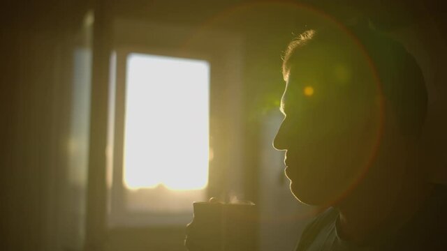 Silhouette of a guy with a mug of hot fresh coffee over a mug, sun flare, camera movement