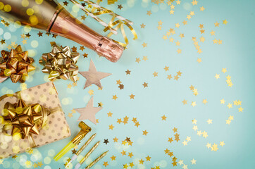 Flat lay champagne bottle with gifts, a golden star, the golden bows and the star confetti on blue pastel background. Flat lay composition for birthday, christmas or wedding.