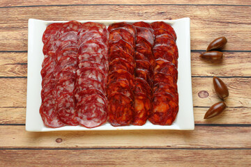 Ration of Iberian ham consisting of chorizo and acorn-fed Iberian sausage in rectangular plate on rustic wooden table and seen from above