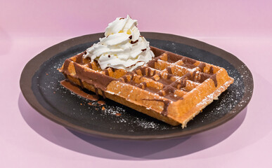 Waffle with chocolate sauce and whipped cream on a black plate.