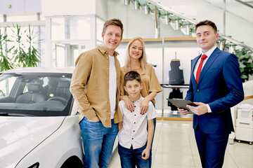 happy young caucasian family now the owners of new beautiful car, they made purchase in cars dealership, get keys from it
