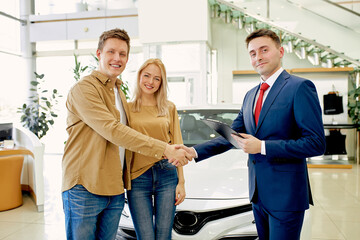 pleasant caucasian customers shake hand to responsive consultant of cars dealership, young family...
