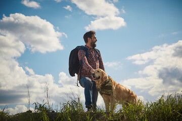 A bearded man in a red shirt with a Golden Retriever against a blue sky. The concept of travel in the open air.