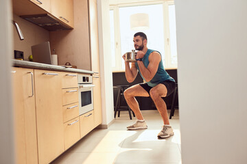 Smiling gentleman doing squats and lifting cooking pot in kitchen