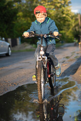 Young boy rides a bicycle through a puddle on a dirt road.