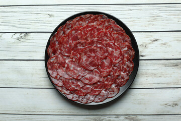 Ration of acorn-fed iberian sausage on black plate on rustic wooden table top view