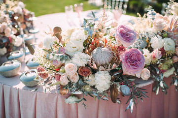 Obraz na płótnie Canvas Presidium, table of the newlyweds. Floral arrangements of pink roses, anthurium, protea, eustoma, carnations, silver leaves. On the table is a pink velvet tablecloth. On the green lawn