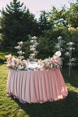 Presidium, table of the newlyweds. Floral arrangements of pink roses, anthurium, protea, eustoma, carnations, silver leaves. On the table is a pink velvet tablecloth. On the green lawn