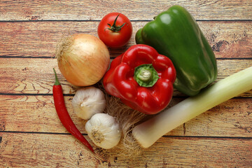 Vegetables still life consisting of leek, garlic, onion, tomato and red and green pepper on rustic wooden table