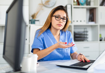 Doctor in uniform is working behind laptop in  hospital