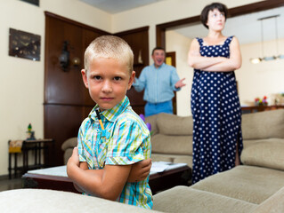 Unhappy small boy sitting  at sofa during his parents quarrelling
