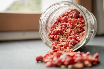 Wild rose hip dry fruit spilled on the black rock surface from glass jar