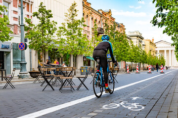 Rider cycling on the road bike in Vilnius city center reopening with open air restaurant and bar...