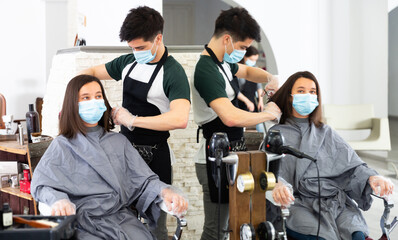 Fototapeta premium Young man professional hairdresser in mask cut female's hair