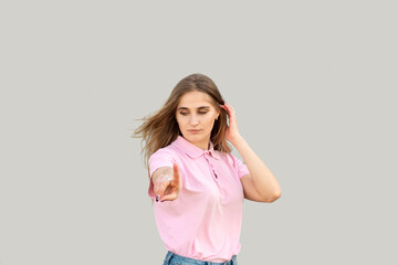 Young girl shows an index finger. Looking away. Dressed in a pink T-shirt and blue jeans. Hair fluttering in the wind. Isolated on gray background.