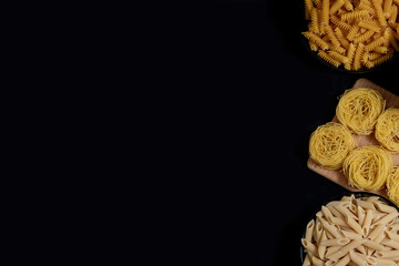 Different types of dry pasta on the plate and in bowls on black background. Space for text, top view