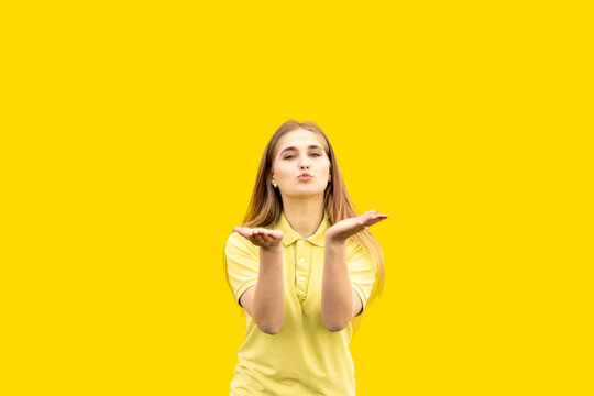 A young girl sends an air kiss to the camera. Shows love. Dressed in a yellow T-shirt. Isolated on yellow background.